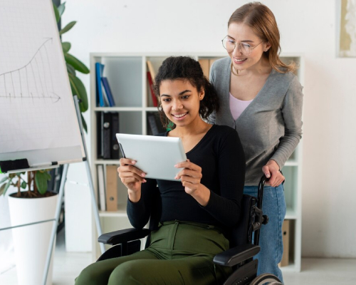 Support worker assisting a young woman in a wheelchair using a tablet, highlighting personalised care and assistance by an NDIS Provider in a home setting.