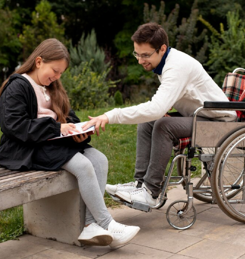 Man in a wheelchair assisting a young girl with reading in a park, highlighting compassionate care, learning support, and inclusive community engagement through NDIS Support Services.